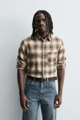 Camisa de corte relajado confeccionada en tejido de algodón con estampado de cuadros en tonos marrones y beige. Presenta cuello solapa, manga larga con puños abotonados, bolsillo plastrón en el pecho y cierre frontal con botones.