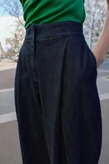Pantalón tipo culotte de tiro alto confeccionado en denim azul oscuro. Presenta pinzas delanteras, pernera ancha y corta, bolsillos laterales ocultos y cierre frontal con cremallera, botón y ganchos.