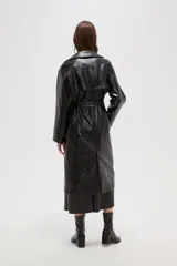 Trinchera de eco-cuero en color bordó, con diseño de doble botonadura, solapas amplias y cinturón ajustable en la cintura. Presenta mangas largas con detalles en los puños y bolsillos laterales.