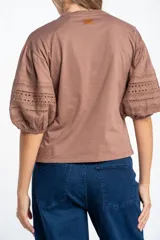 Remera negra de algodón con mangas cortas abullonadas que presentan detalles de encaje bordado y calado en los extremos.