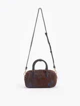 Cartera tipo baulito de cuero descarne vacuno con textura rayada en tonos marrón y azul. Presenta manijas cortas, cierre superior y un charm metálico dorado en forma de mariquita colgando de un tag de cuero. Incluye correa larga desmontable y regulable.
