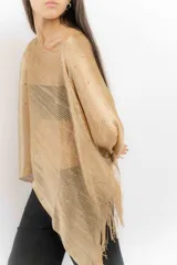 Poncho de tejido de punto metalizado en color dorado, con diseño amplio y flecos en el borde inferior. Presenta apliques sutiles de piedras y un estilo holgado.