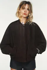 Cazadora tipo bomber de Zara confeccionada en piel de ante 100%. Presenta cuello redondo, cierre frontal con cremallera metálica, bolsillos delanteros con solapa y bajo con acabado elástico.
