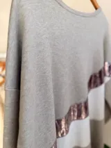 Buzo de tejido de punto con diseño oversize y calce relajado. Presenta un diseño de bloques de color en tonos neutros con una franja diagonal central en material metalizado brillante. Cuenta con cuello redondo y mangas largas con puños acanalados.