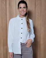Camisa de algodón color blanco, con cuello mao, cierre frontal de botones oscuros y detalle de volados sutiles a lo largo de la botonadura. Presenta mangas largas con frunces en los hombros.