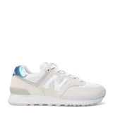 Championes urbanos New Balance modelo 574, color beige claro con detalles en blanco y azul metalizado en el talón. Confeccionados en una combinación de gamuza y malla, cuentan con el logo N característico en los laterales y entresuela con tecnología de amortiguación.