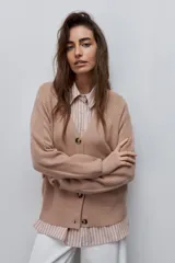 Cardigan de punto color beige, con escote en V, cierre frontal con botones oscuros y mangas largas con detalles de tejido en relieve.