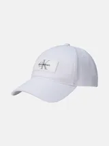 Gorra de béisbol blanca de algodón con visera curva y cierre ajustable con hebilla. Presenta un parche rectangular de silicona en el frente con el logo de Calvin Klein en color gris.
