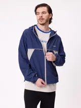 Rompevientos Rusty con capucha, diseño bicolor en azul marino y gris, cierre frontal y logo bordado en el pecho.