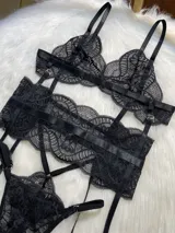 Conjunto de lencería de cuatro piezas en encaje negro, compuesto por bralette, tanga con tiras regulables, portaligas y ligas para piernas.