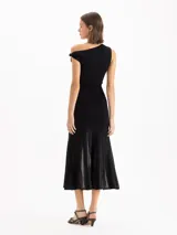 Vestido largo negro de corte sirena con escote asimétrico caído en un hombro. Presenta falda con paneles transparentes y plisados verticales a partir de las rodillas.
