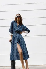 Vestido midi azul marino con rayas blancas, cuello solapa, escote en V y cierre frontal con botones. Cuenta con mangas abullonadas por debajo del codo con puños anchos a contraste, cinturón ajustable del mismo tejido con hebilla metálica y falda evasé.