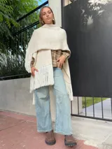 Ruana tejida de lana en color crudo, con diseño de flecos en los bordes. Es una prenda versátil y abrigada, ideal para complementar diversos looks.