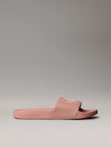Ojotas tipo slide Calvin Klein Jeans, color rosado, con banda superior de lona de algodón reciclado y logo de la marca estampado en blanco. Presentan suela de EVA con plantilla ergonómica moldeada.