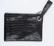 Sobre de cuero negro con textura tipo croco, cierre superior con cremallera y tira de cuero para la muñeca.