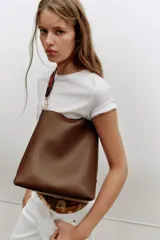 Bolso de hombro tipo saca en color marrón, con diseño minimalista y cierre de clip metálico. Incluye una correa de hombro con detalles troquelados en contraste y herrajes dorados.