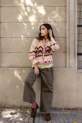 Saco tejido a mano con diseño jacquard geométrico en tonos rosa, amarillo y bordó. Presenta cuello a la base, cierre frontal con botones y silueta corta.