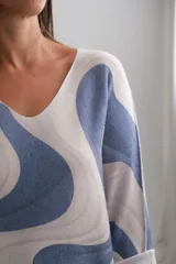 Sweter de punto con diseño de ondas abstractas en tonos azul y beige, escote en V y mangas largas con puños doblados.