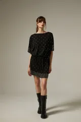 Vestido corto de poliéster color negro con escote a la base, mangas cortas y diseño holgado. Cuenta con detalles de tachas metálicas plateadas distribuidas por la prenda y agrupadas en el dobladillo y los puños.