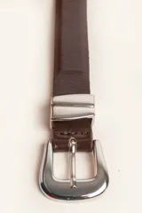 Cinturón de cuero liso color marrón oscuro con hebilla plateada y pasador metálico decorativo.