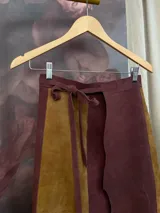 Falda larga de cuero en diseño de paneles bicolor, combinando tonos marrón y bordó. Presenta cintura ajustable con lazo y un diseño de borde lateral irregular con tajos.