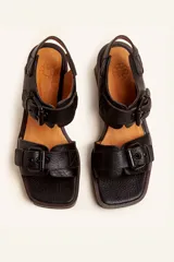 Sandalias de cuero negro con taco bloque de madera tallada, tiras con hebillas grandes y punta cuadrada.