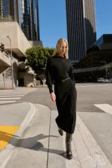 Vestido midi de punto en color negro, con cuello barco y mangas largas con sisa ancha. Presenta una cintura entallada con un cinturón fino incorporado con hebilla metálica dorada.