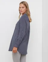 Camisa de corte largo y holgado, con estampado de rayas verticales en azul marino y blanco. Presenta cuello con solapa, cierre frontal con botones, bolsillo en el pecho y mangas largas con puños abotonados.