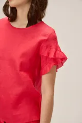 Blusa de lino color rosado, de corte recto y holgado, con cuello redondo y mangas cortas adornadas con volados.