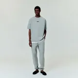 Camiseta gris con logo "Essentials Fear of God" en el pecho y etiqueta de goma en la parte posterior. Corte oversize.