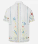 Camisa blanca de lino y algodón, de corte comfort, cuello inglés y abotonado frontal. Presenta manga corta y un bordado floral multicolor con motivos de aves y flores.