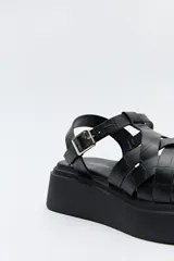 Sandalia negra con plataforma bicolor y capellada de tiras entrelazadas con textura símil reptil. Tiene hebilla metálica lateral para ajustar el calce y suela de goma.