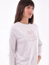 Remera de manga larga color crema con cuello redondo y un estampado central de un ramo de flores rosadas y naranjas en un jarrón azul oscuro.