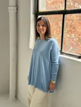 Sweater de punto color celeste, con cuello redondo, corte holgado y mangas largas con puños acanalados. Presenta un detalle de costura vertical central en el frente.