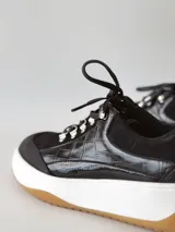 Zapatillas deportivas negras de cuero, con cordones y suela de goma blanca con base marrón.