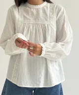 Blusa blanca de corte holgado con cuello redondo, mangas largas con puños elásticos y detalles de puntillas verticales en el frente.