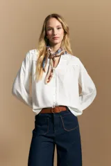 Camisa de manga larga color blanco, con cuello mao y escote en V. Presenta frunces en el canesú, cierre frontal con botones y mangas amplias con puños abotonados.