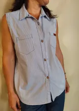 Musculosa tipo camisa con cuello camisero, cierre frontal de botones y dos bolsillos delanteros en el pecho. Diseño a rayas verticales en tonos celeste y blanco.
