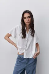 Camisa negra de manga corta, con cuello mao y cierre frontal de botones, de silueta amplia y tejido liviano con textura sutil.