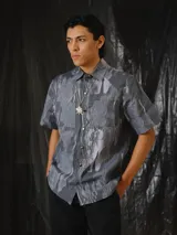 Camisa de manga corta con estampado abstracto en tonos grises, cuello clásico, bolsillos frontales aplicados y cierre frontal de botones a presión.