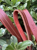Llavero de cuero en formato de tira con diseño minimalista, confeccionado en cuero genuino marrón con interior en contraste color fucsia, pespuntes rosados y herrajes metálicos envejecidos con gancho tipo mosquetón.