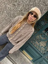 Saco tejido de punto con diseño de ochos y trenzas, color azul marino. Presenta cierre frontal con botones en contraste de color turquesa y un delicado bordado a mano en el pecho.