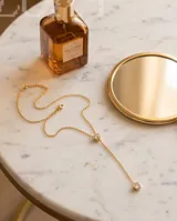 Collar estilo corbatero de acero dorado con dos circonias engarzadas en formato circular, una en el centro y otra en el extremo inferior.