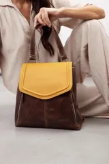 Mochila de cuero vacuno marrón con acabado pulido, solapa en forma de V y costuras decorativas. Cuenta con cremalleras laterales y asas ajustables.
