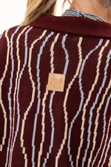 Buzo de punto color vino con diseño de rayas verticales irregulares en tonos claros. Presenta cuello polo con cierre frontal de tres botones, mangas largas con puños acanalados y corte holgado.