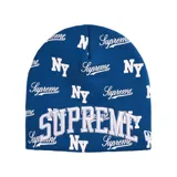 Gorro de lana tipo beanie color azul con estampado integral de logotipos Supreme y NY en color blanco. Presenta un bordado destacado de la palabra SUPREME en la parte frontal.