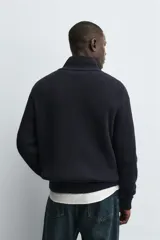 Chaqueta de punto de algodón con textura perlada, corte regular fit, cuello subido y cierre frontal con cremallera. Presenta mangas largas con puños y ruedo en rib.