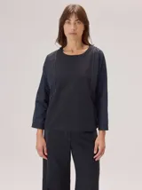 Camisa de manga larga con cuello redondo, confeccionada en una combinación de algodón y tencel. Presenta un diseño minimalista con costuras decorativas visibles en contraste que recorren el frente y los laterales.