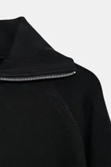 Chaqueta de felpa negra con cuello solapa, manga larga con puño, bolsillos de plastrón en el delantero y cierre frontal con cremallera.