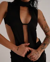 Conjunto de dos piezas compuesto por un top sin mangas con cuello alto y diseño de aberturas laterales y frontales, y una minifalda ajustada a juego. Ambas prendas están confeccionadas en tela satinada de color negro.